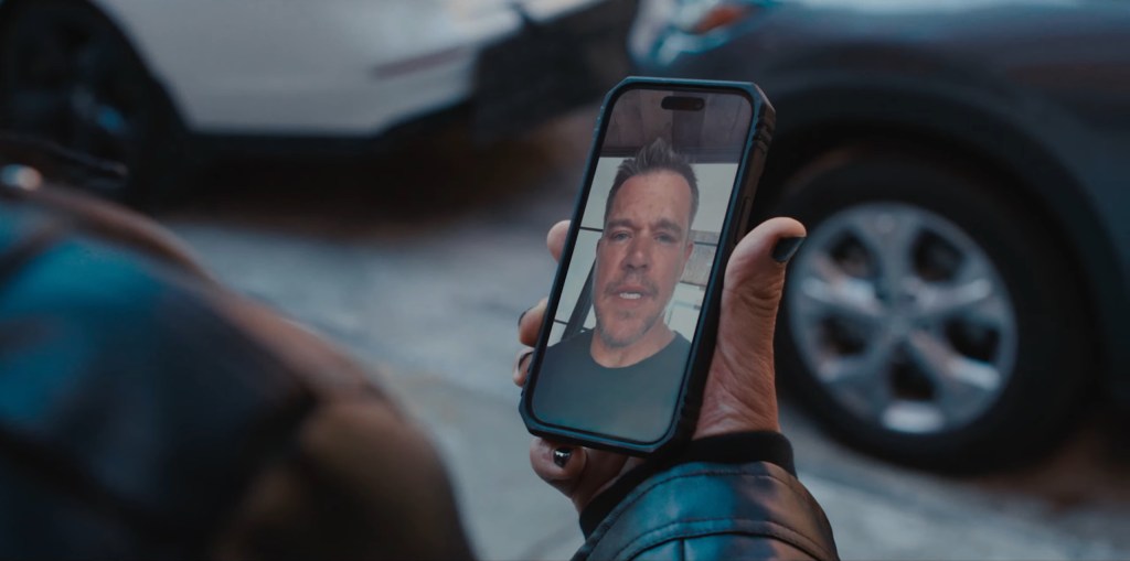 A hand holding a smartphone showing Matt Damon on screen.