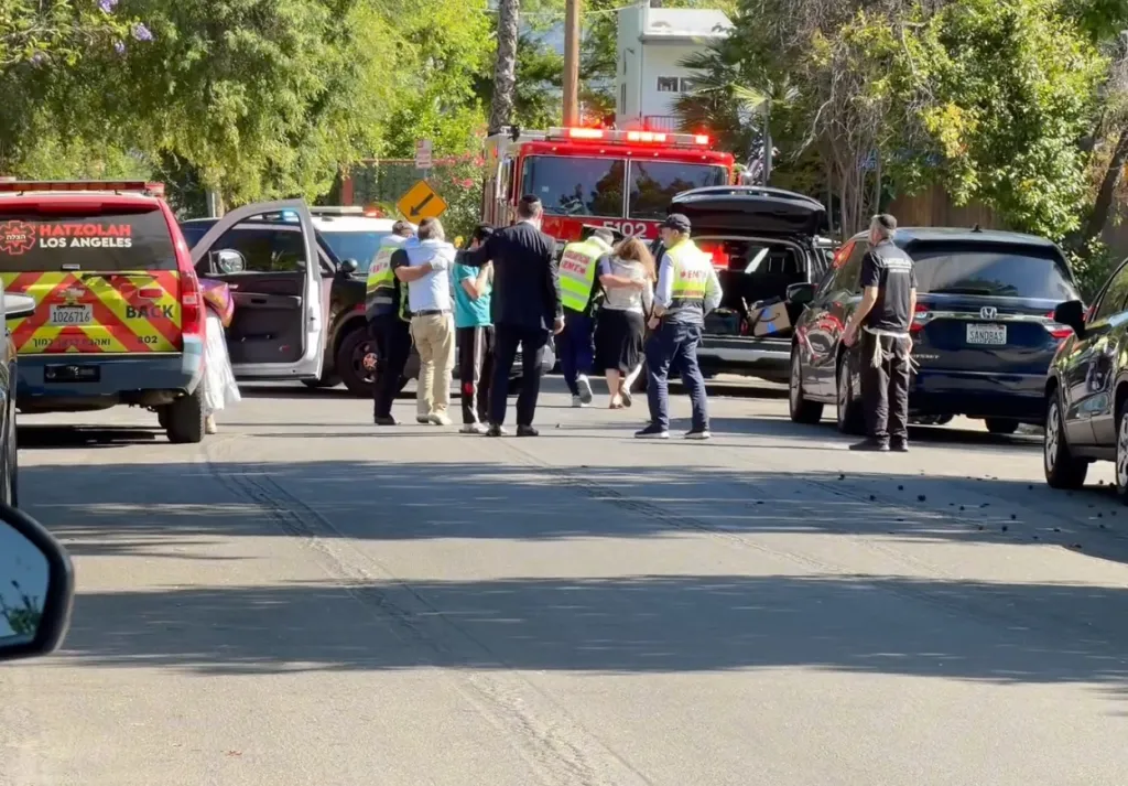First responders and civilians gather near emergency vehicles on a street.