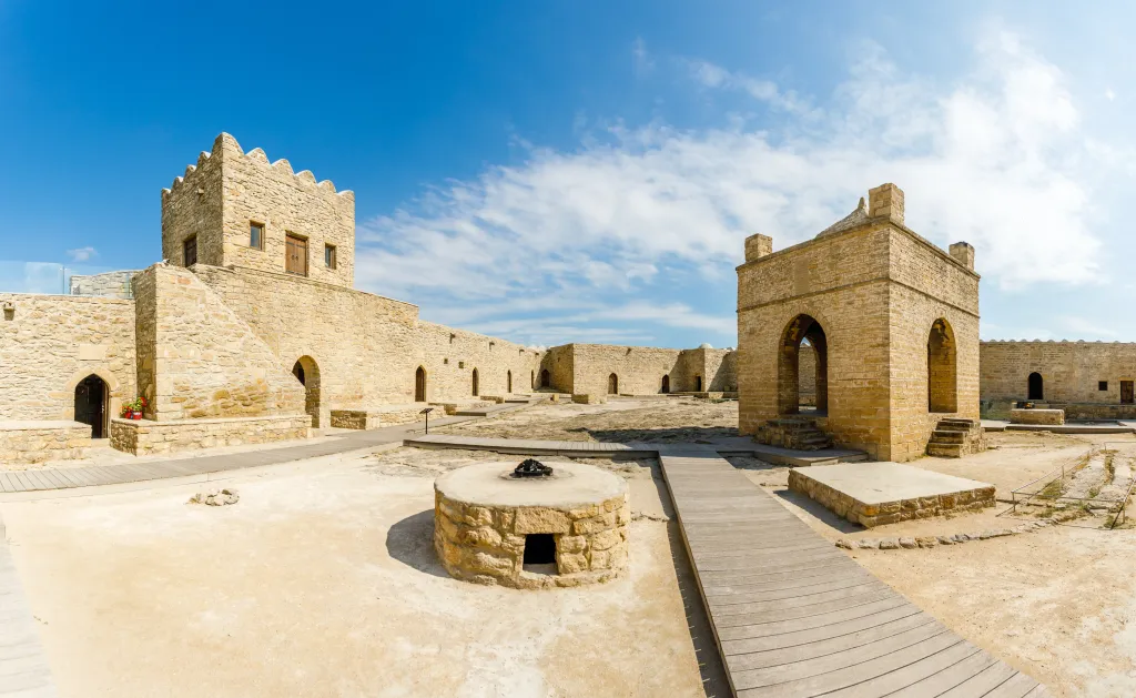 The inner yard of the ancient stone Atashgah Zoroastrian fire temple in Baku, Azerbaijan, features a central fire pit and several stone buildings with arched doorways.