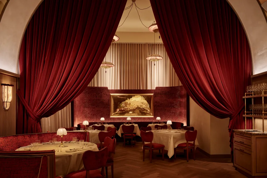 The dining room of Tao's new Crane Club Restaurant, featuring red velvet chairs and curtains, white tablecloths, and warm lighting.