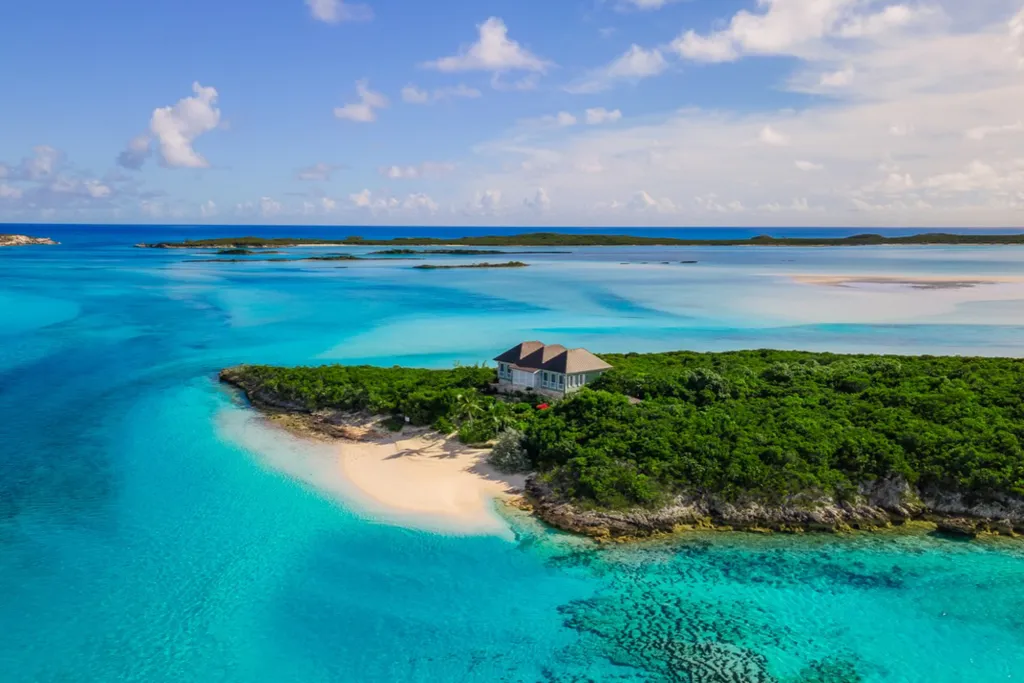 Aerial view of a private island in the Bahamas with a house, sandy beach, and turquoise water.