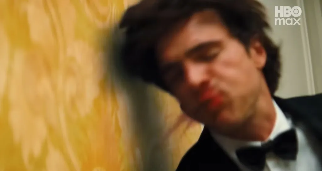 Jacob Elordi with his eyes closed, in a black suit with a bow tie, slumped against a yellow wall.