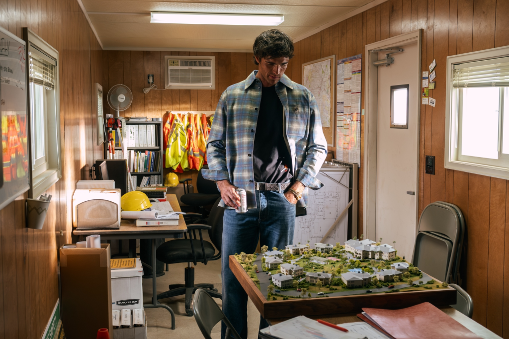 Jacob Elordi as Nate Jacobs in a plaid shirt looking at a miniature neighborhood model.