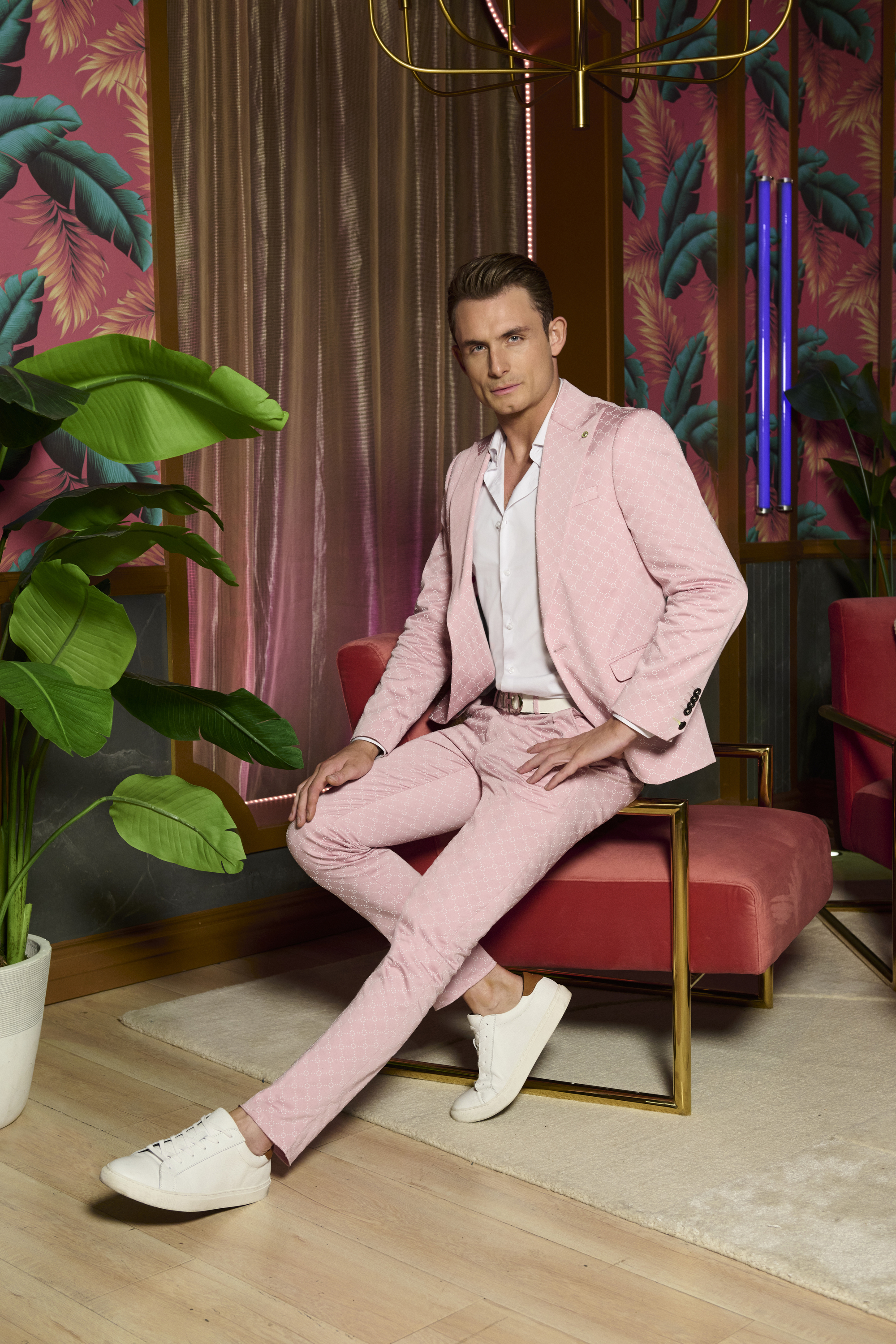James Kennedy making eye contact, dressed in a pink suit and white sneakers, sitting indoors.