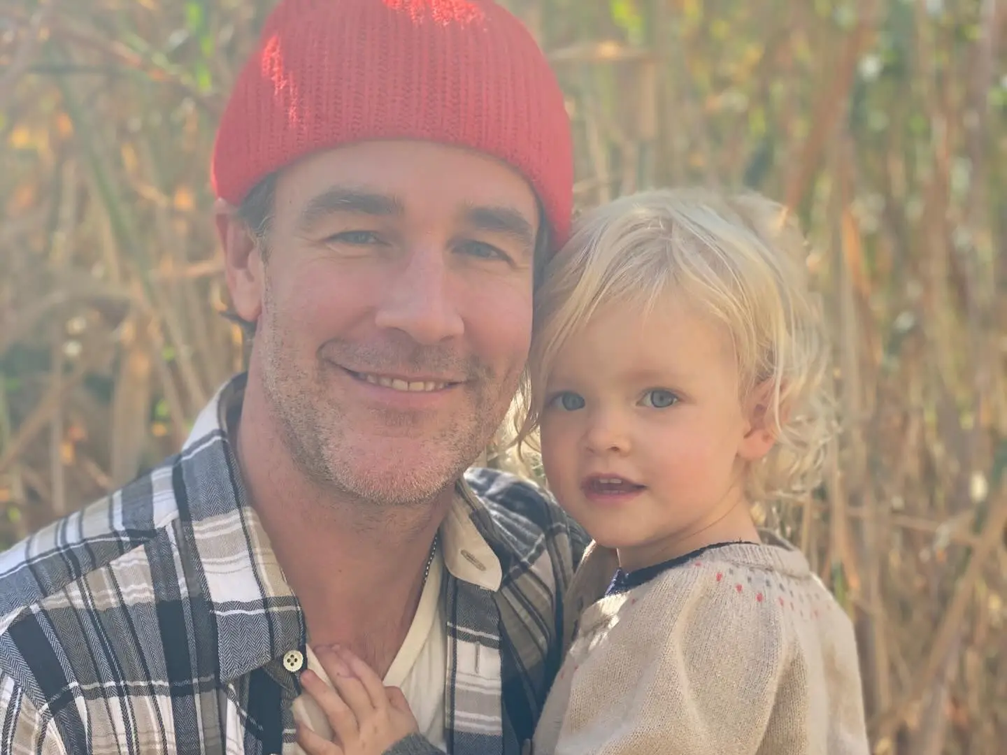 James Van Der Beek, wearing a red beanie, holds a blonde child.