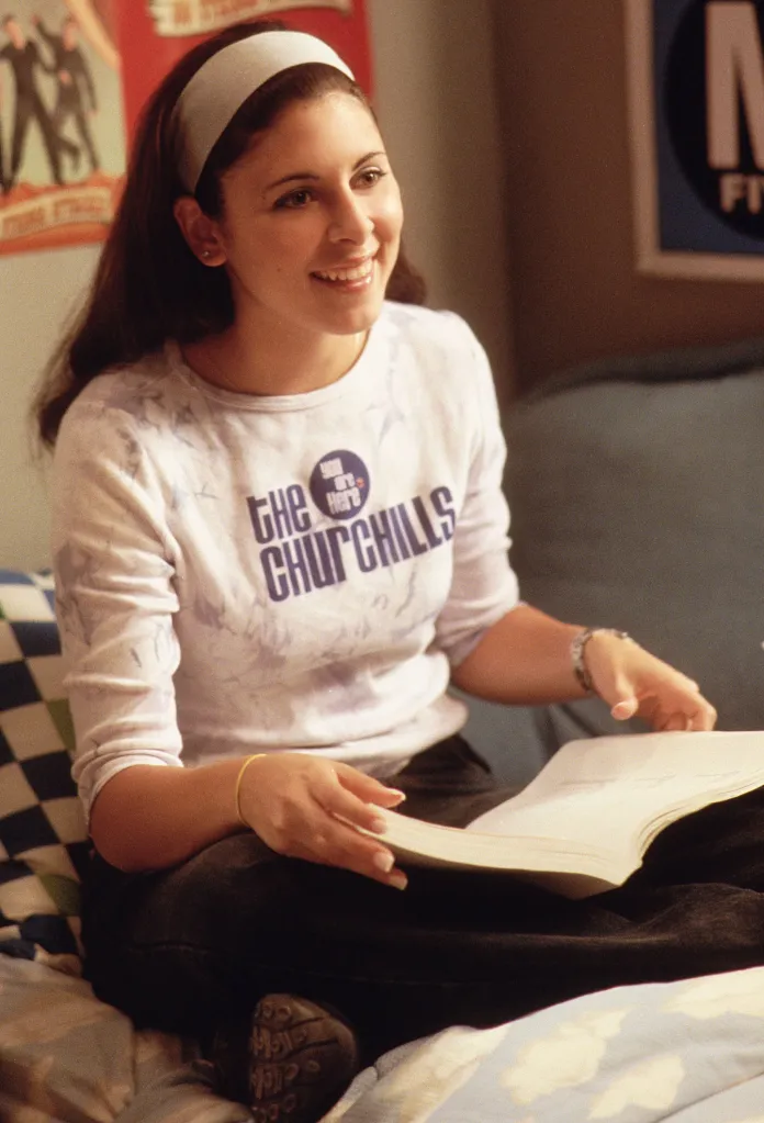 Jamie-Lynn Sigler as Meadow Soprano smiles while sitting with a book in 