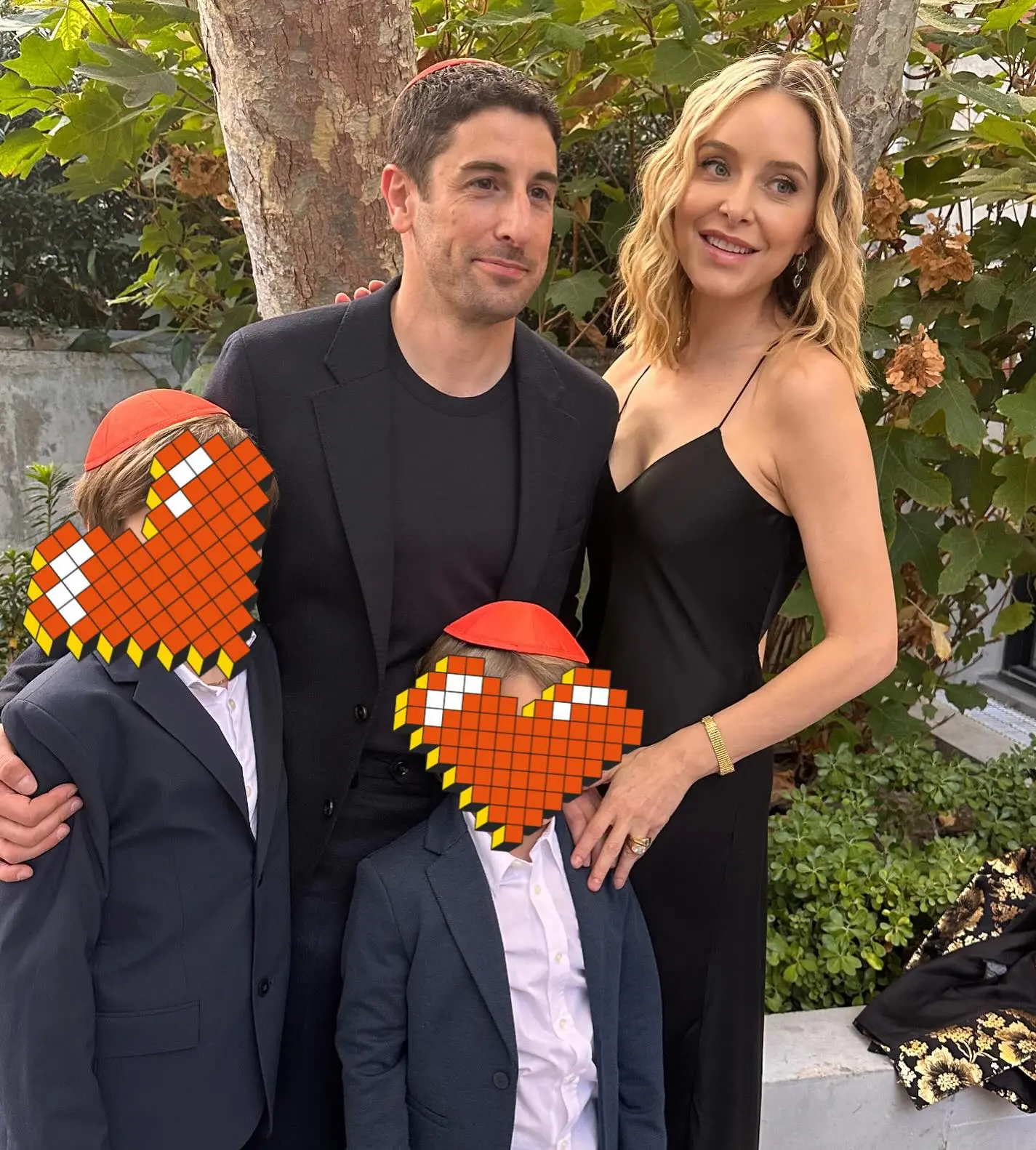 Jason Biggs and Jenny Mollen pose for a photo with their two children, whose faces are obscured by pixelated heart emojis.