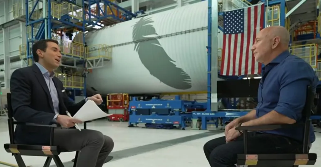 Jeff Bezos being interviewed in front of a rocket with the Blue Origin feather logo.
