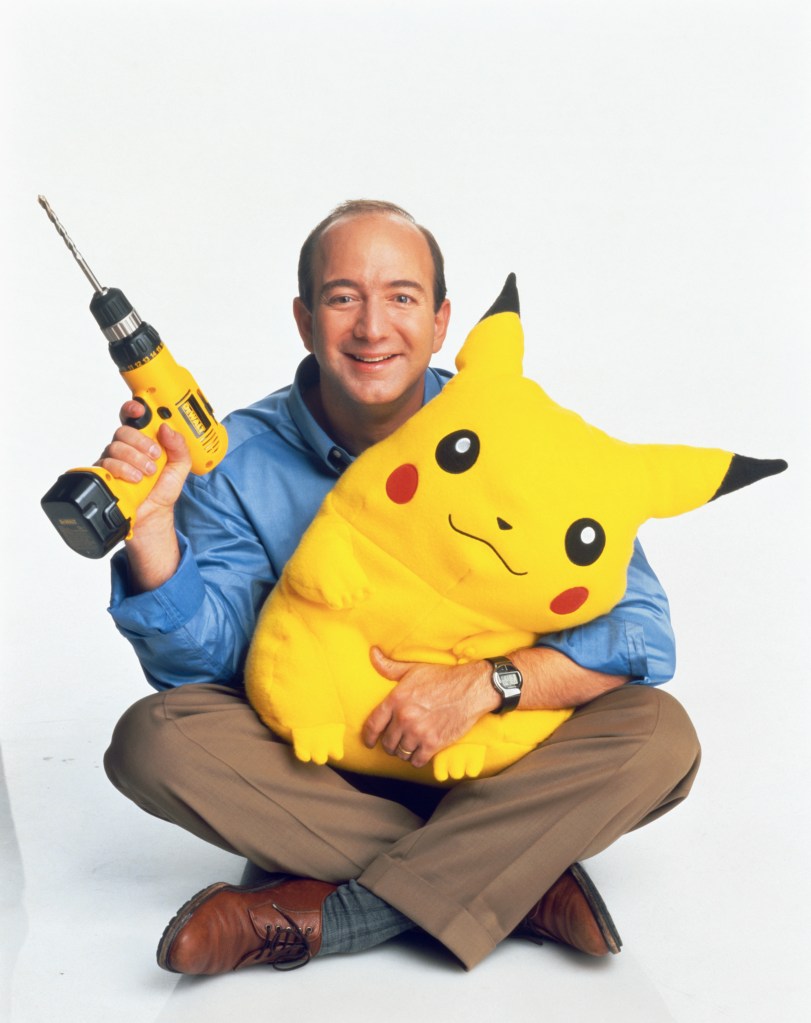 Jeff Bezos, holding a drill and a Pikachu stuffed animal. He wears a blue shirt and brown pants.