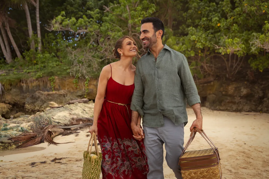 Jennifer Lopez as Jackie Cruz and Brett Goldstein as Daniel Blanchflower walking hand-in-hand on a beach.