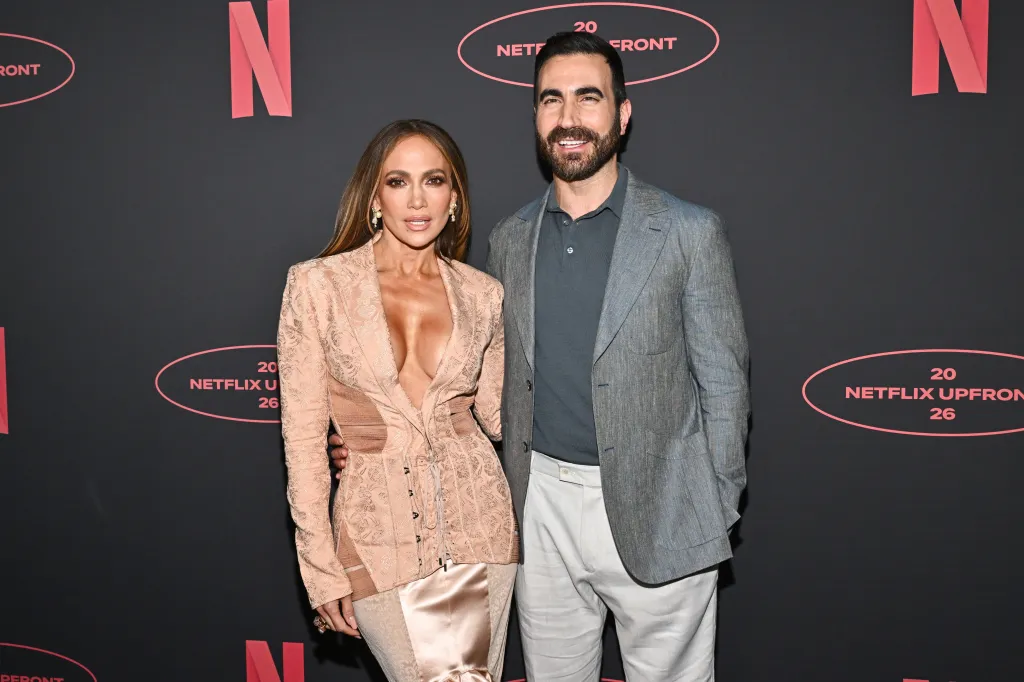 Jennifer Lopez in a light peach blazer and Brett Goldstein in a gray suit jacket pose for a photo at the Netflix Upfront.