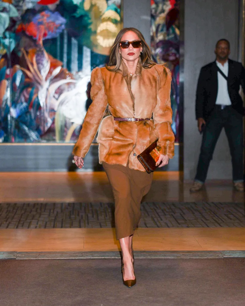 Jennifer Lopez wearing a brown fur coat, brown skirt, brown heels, and sunglasses, holding a brown handbag.