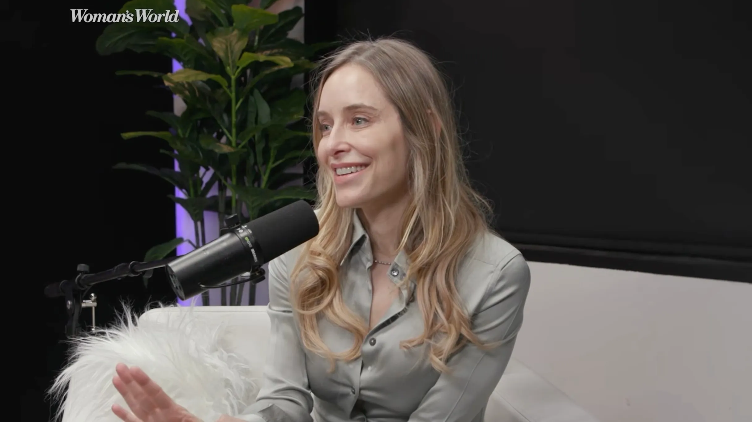 Jenny Mollen, speaking into a microphone while sitting on a white couch.