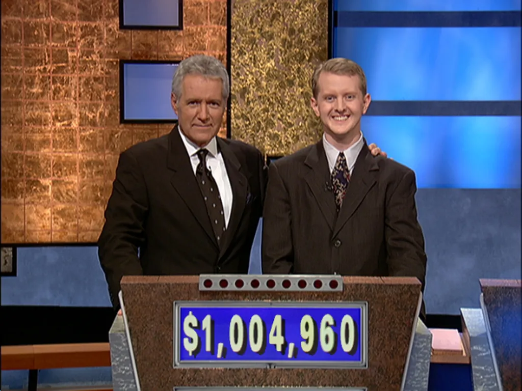 Alex Trebek and Ken Jennings smiling on the Jeopardy set, with winnings of $1,004,960 displayed on a monitor.