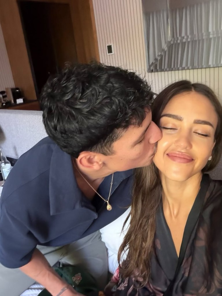 Jessica Alba with eyes closed, smiling as Danny Ramirez kisses her on the cheek.