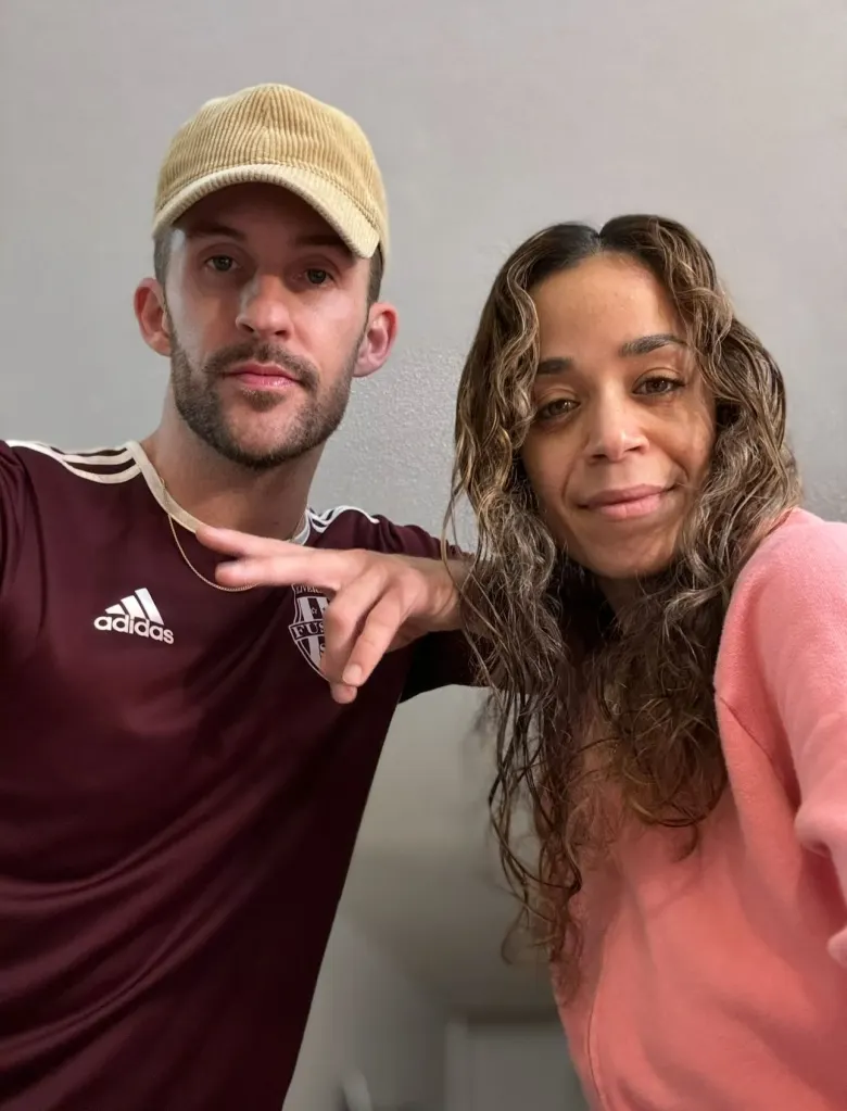 A man in a baseball cap and a woman with curly hair smile for a selfie.