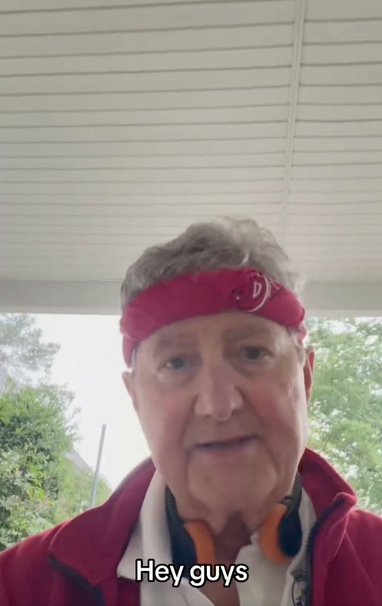 Close-up of a man wearing a red bandana and red jacket, speaking to the camera.