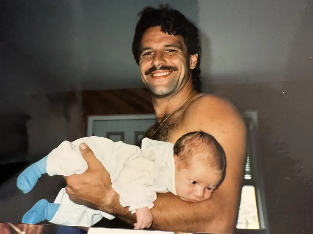 John Pisano Jr. smiling and holding an infant.