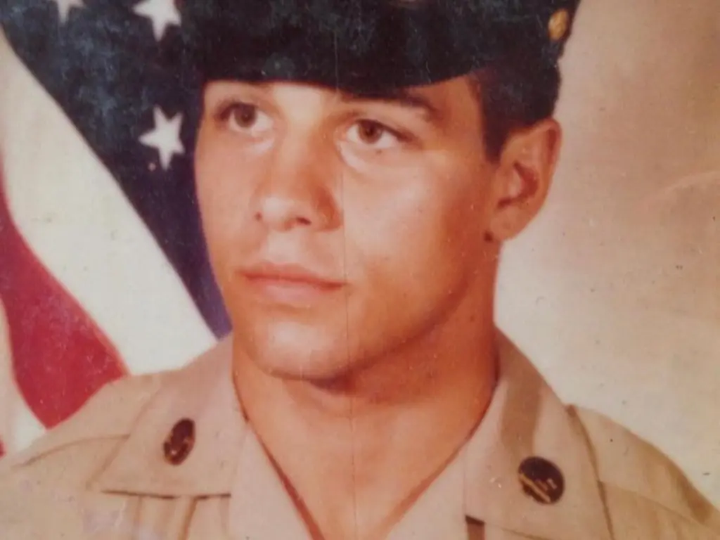 John Pisano Jr. in military uniform, in front of an American flag.