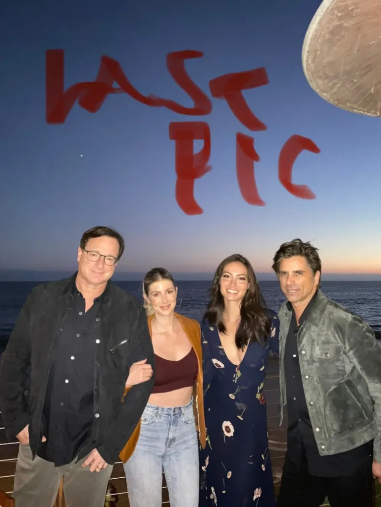 Bob Saget and John Stamos with two women, standing by the ocean at sunset, with the words 