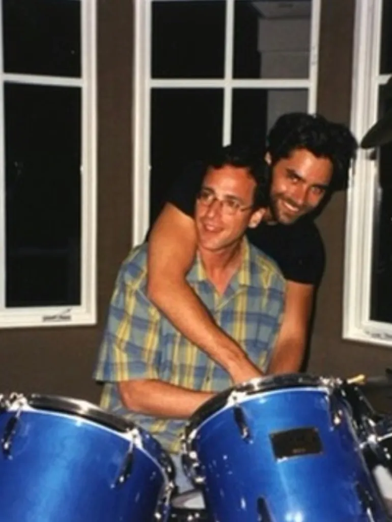 Bob Saget and John Stamos behind a drum kit.