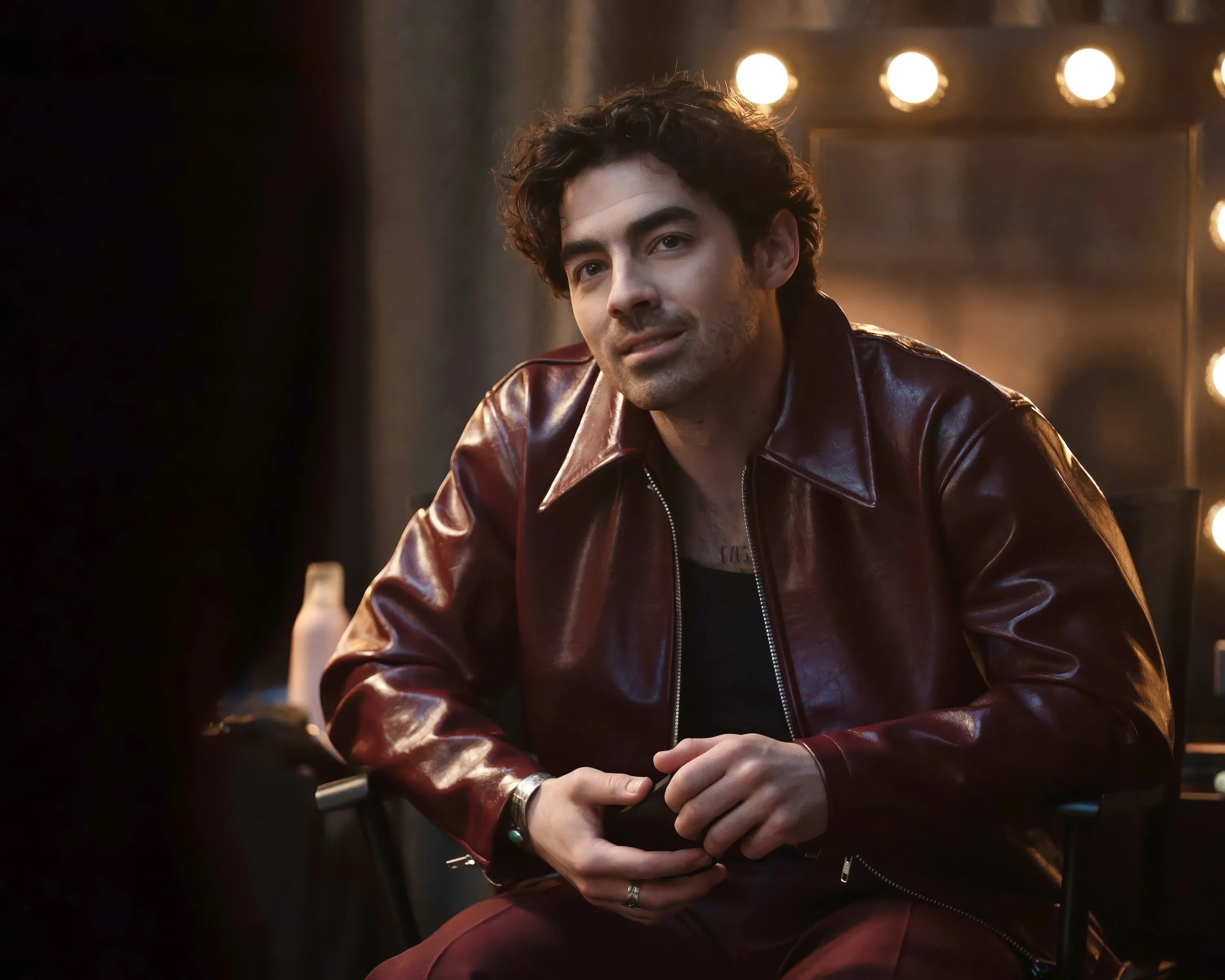 Joe Jonas in a maroon leather jacket, looking towards the camera.