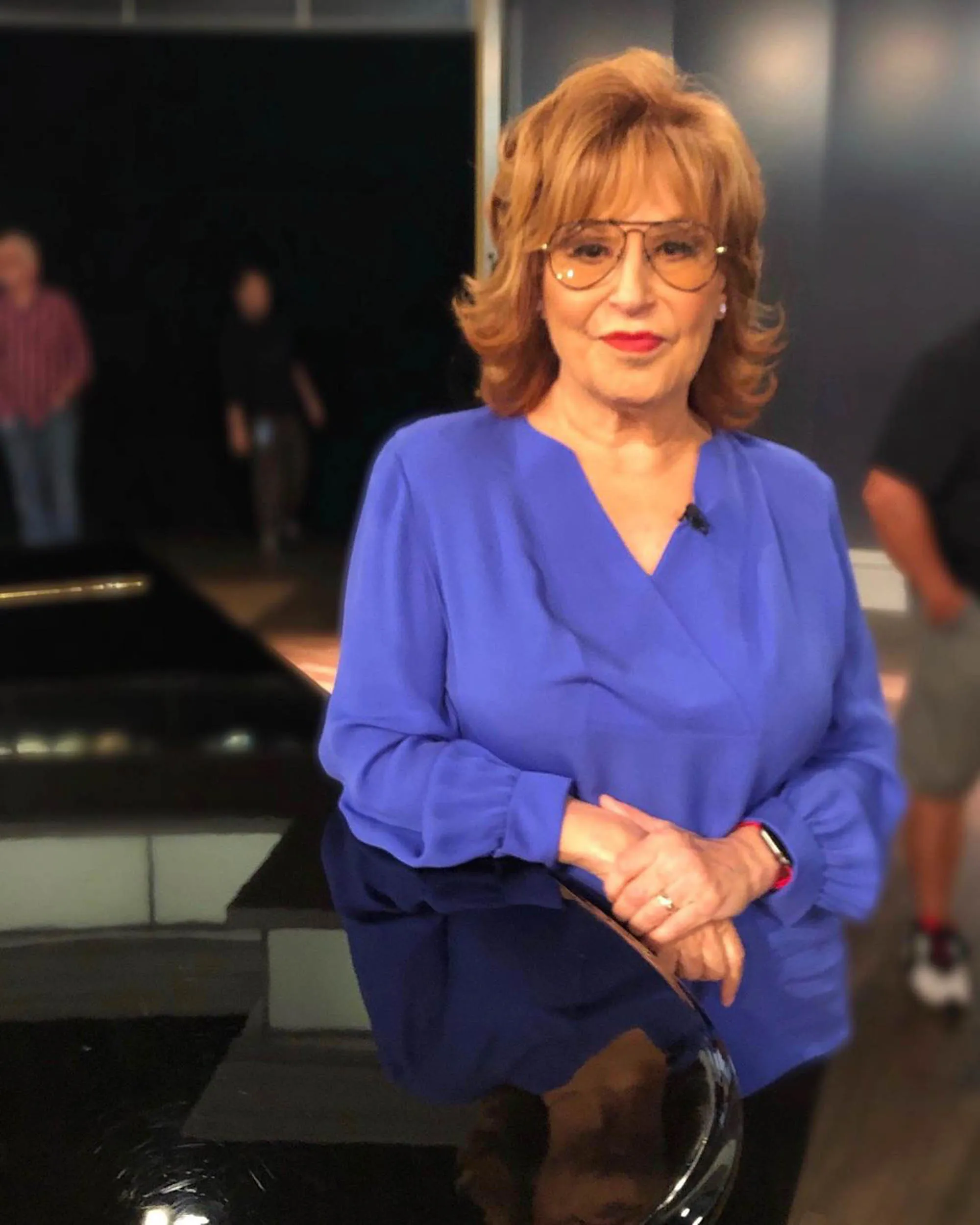 Joy Behar wearing a blue shirt and eyeglasses, smiling.