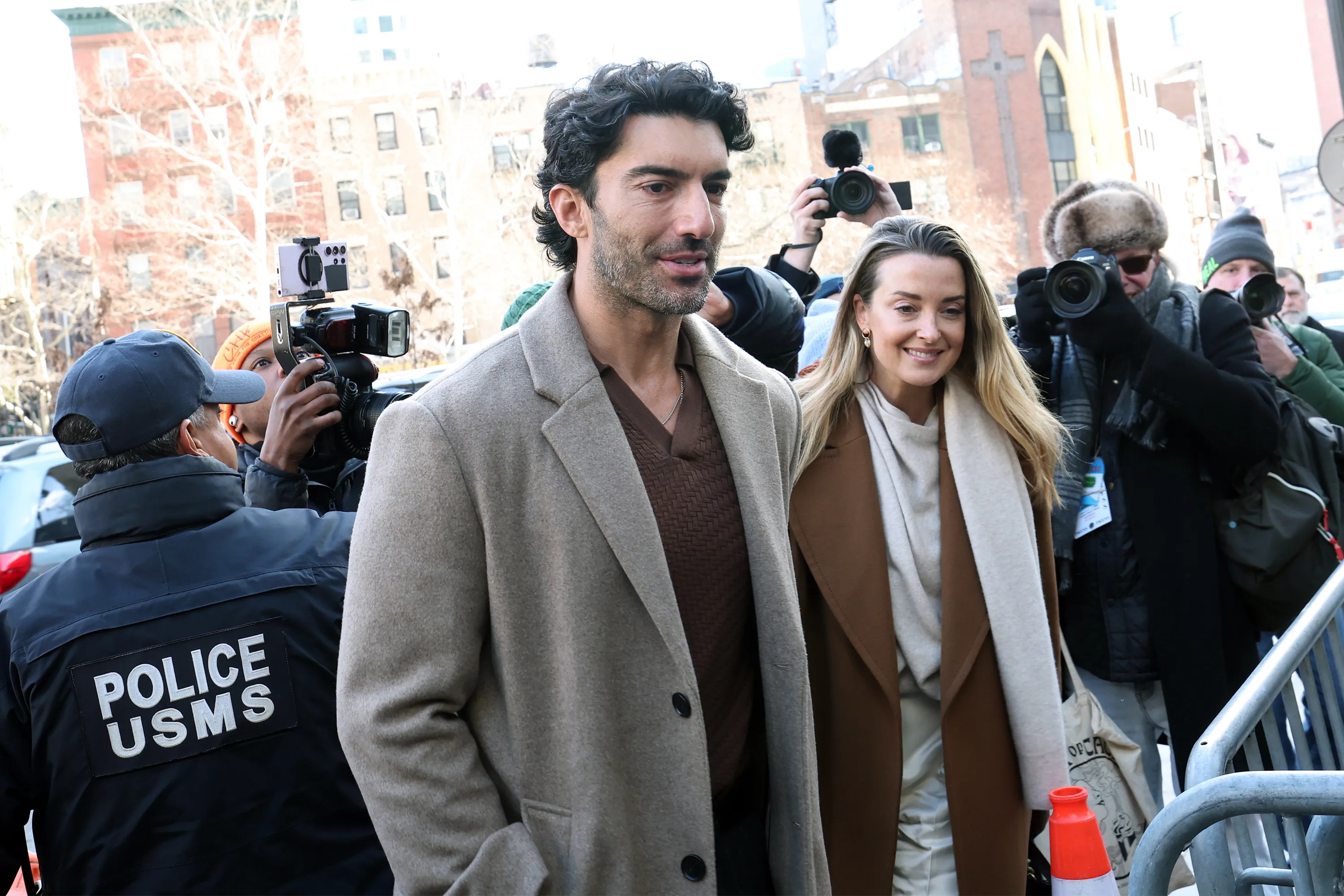 Justin Baldoni and a woman walking past press photographers.