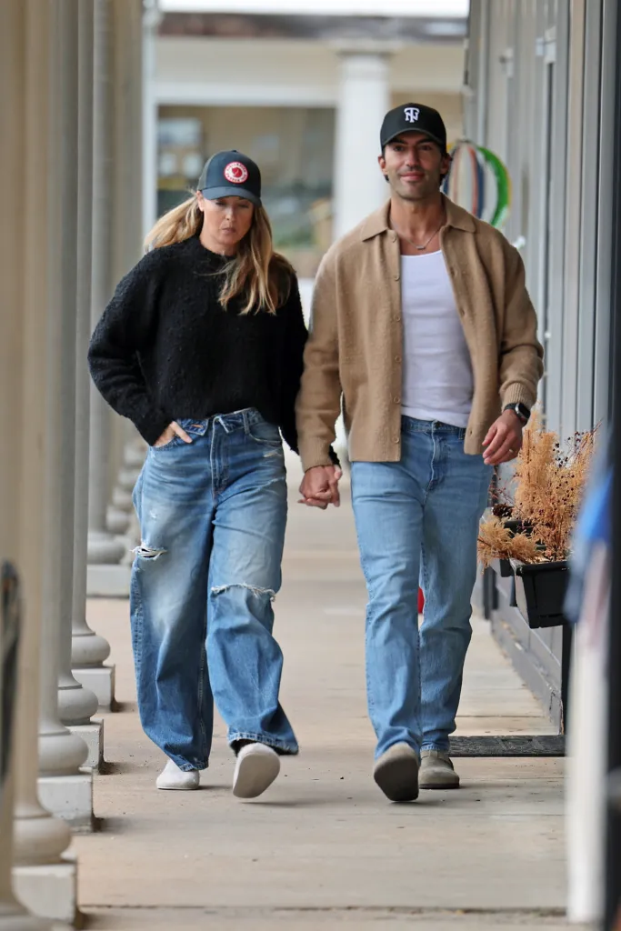 Justin Baldoni and his wife Emily, holding hands, walk past a row of pillars.