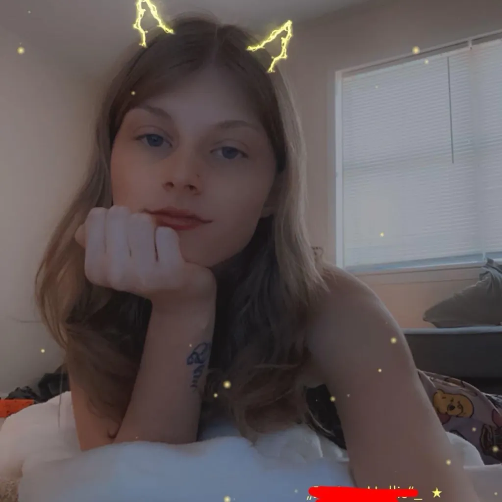 Karen Deann Hollis, a woman with long blonde hair and blue eyes, rests her chin on her hand and looks at the camera while wearing glowing cat ears.