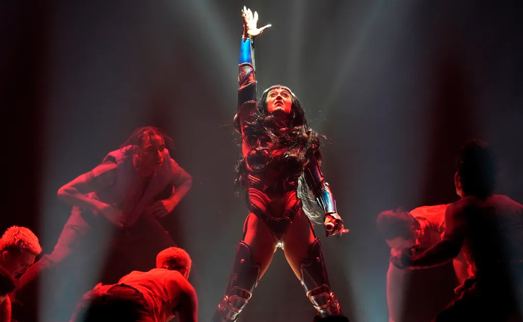 Katy Perry performs in a metallic red and black bodysuit with dancers on stage.