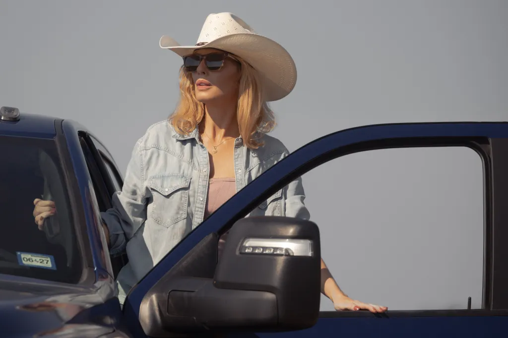 Kelly Reilly as Beth Dutton wearing a cowboy hat and sunglasses, leaning against a truck.