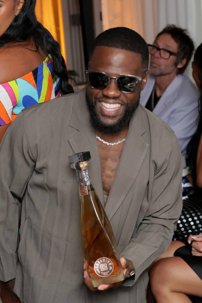 Kevin Hart smiling and holding a bottle of Gran Coramino tequila at the Sports Illustrated Race Weekend Kickoff.