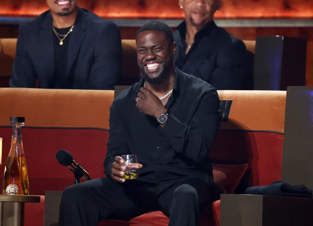 Kevin Hart laughing while sitting on a red couch at the Netflix Is A Joke Festival.