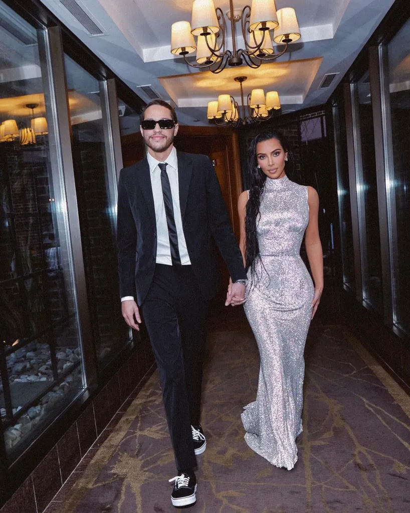 Kim Kardashian in a silver dress and Pete Davidson in a suit holding hands.