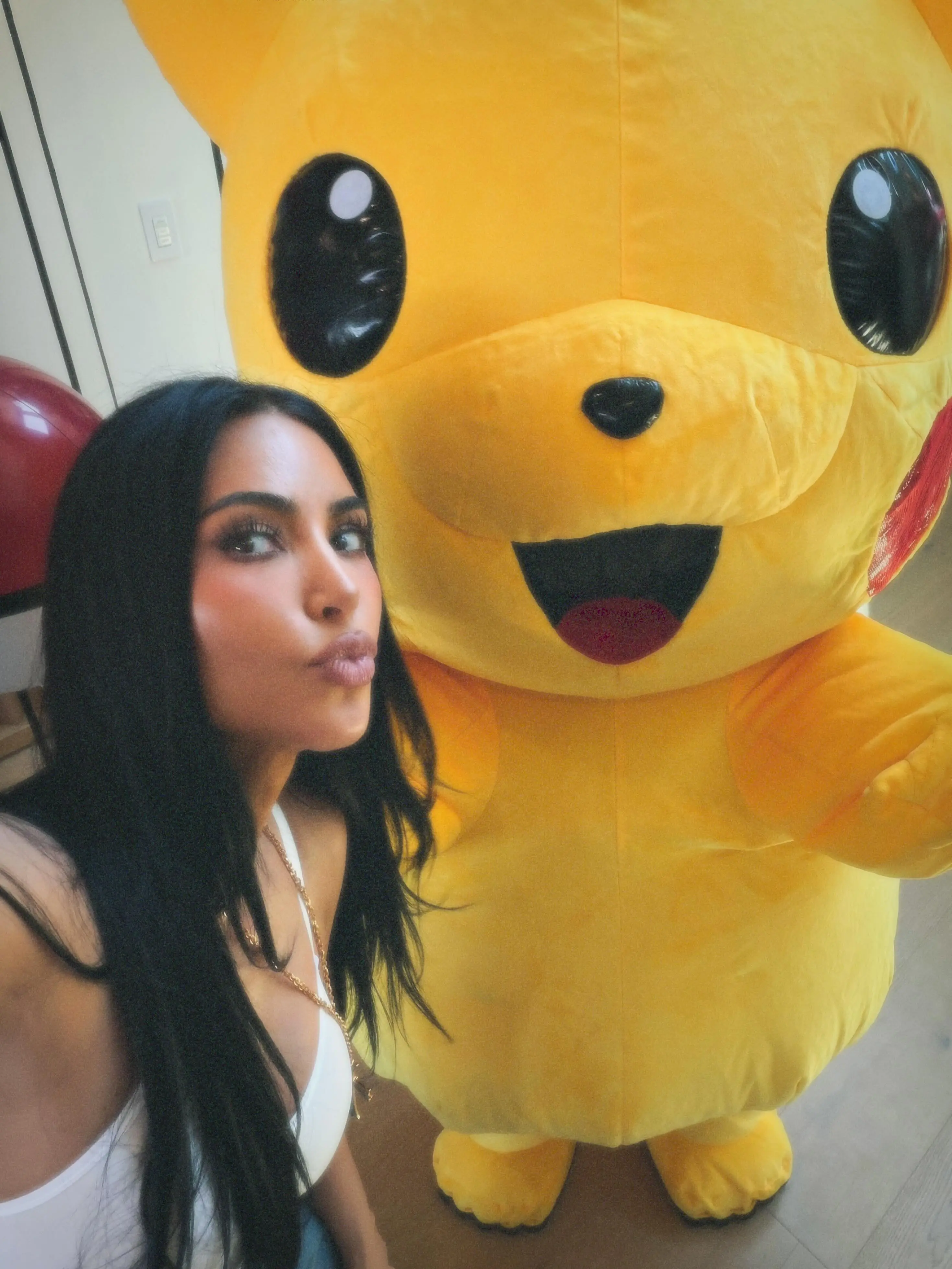 Kim Kardashian making a kissy face next to a large Pikachu mascot.