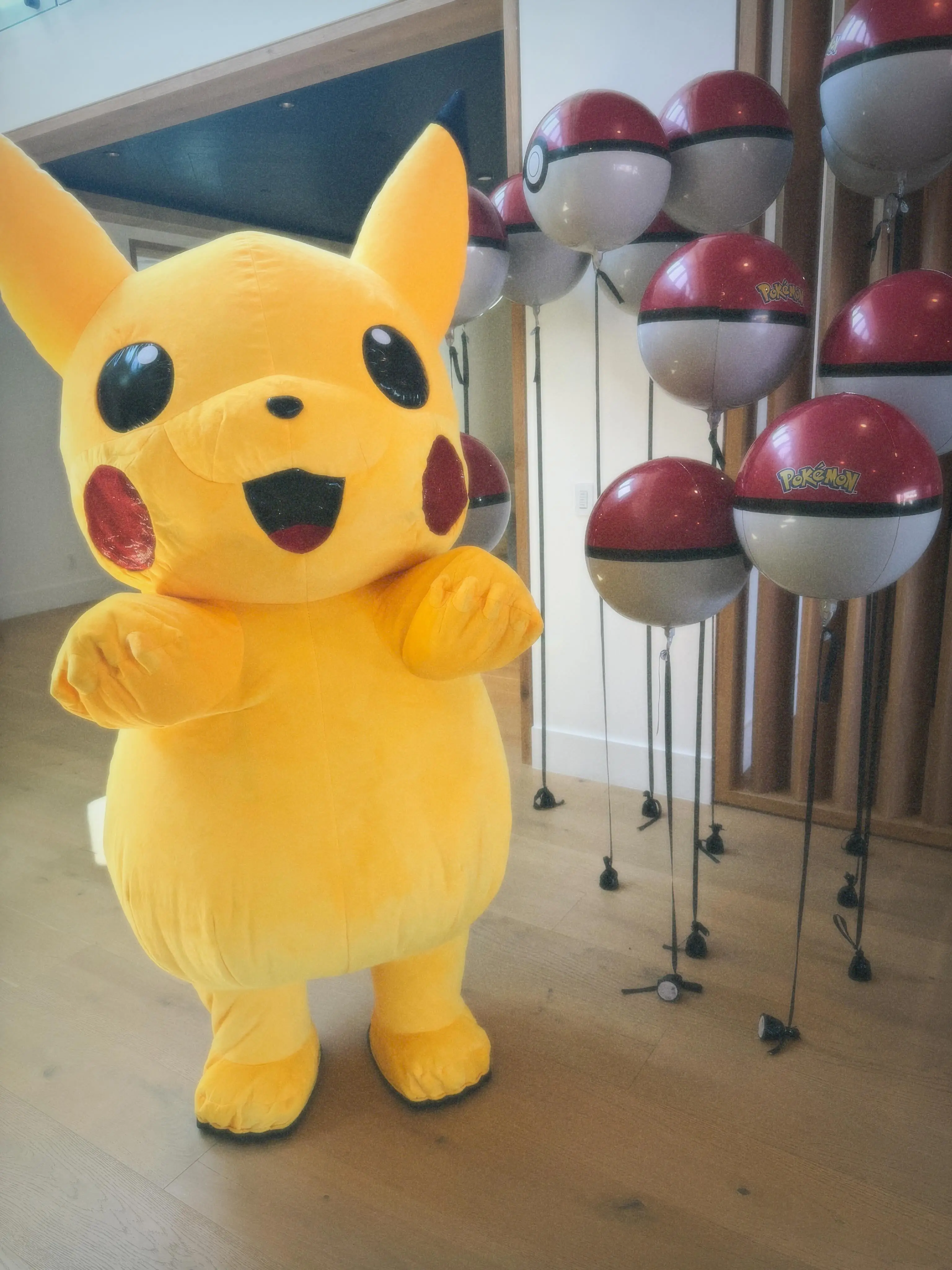 A Pikachu costume stands next to red and white Pokeball balloons.