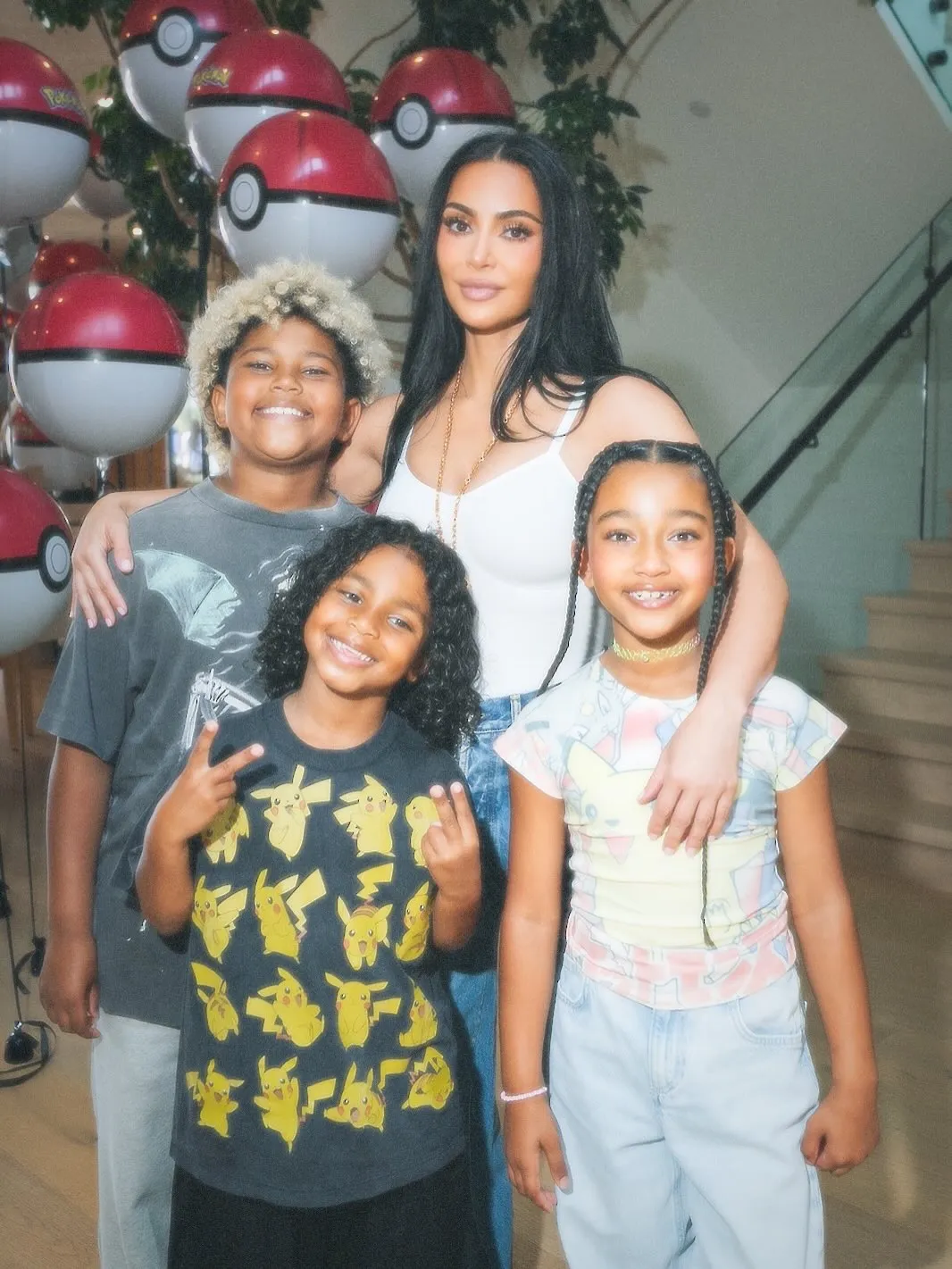 Kim Kardashian poses with children in front of Pokeball balloons at a Pokemon-themed party.