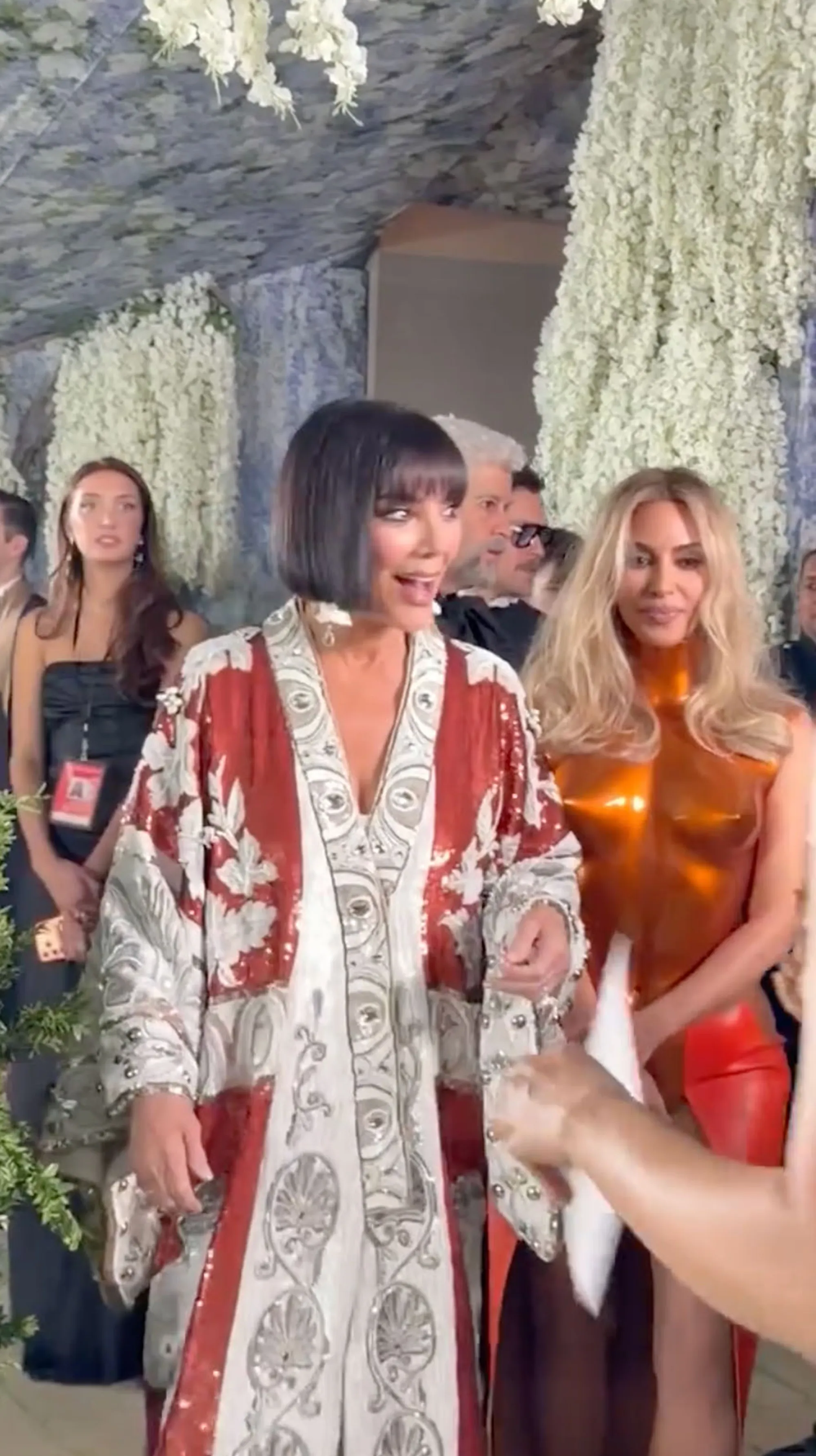 Kris Jenner in a red and white ornate robe-like garment and Kim Kardashian in a copper-colored top and red bottom at the Met Gala.