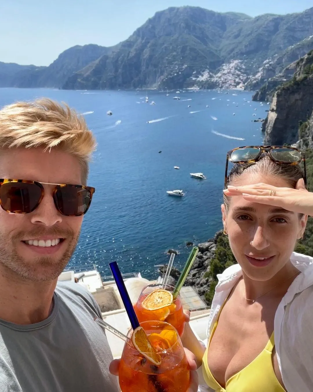 Kyle Cooke and Amanda Batula holding drinks with a scenic coastline in the background.