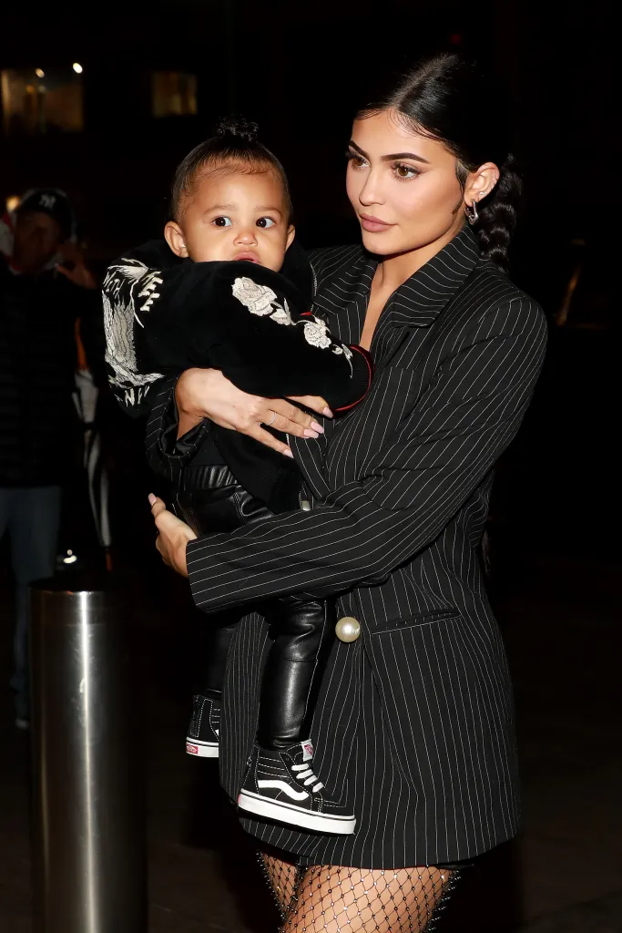 Kylie Jenner holding her daughter, Stormi Webster, both wearing black outfits.