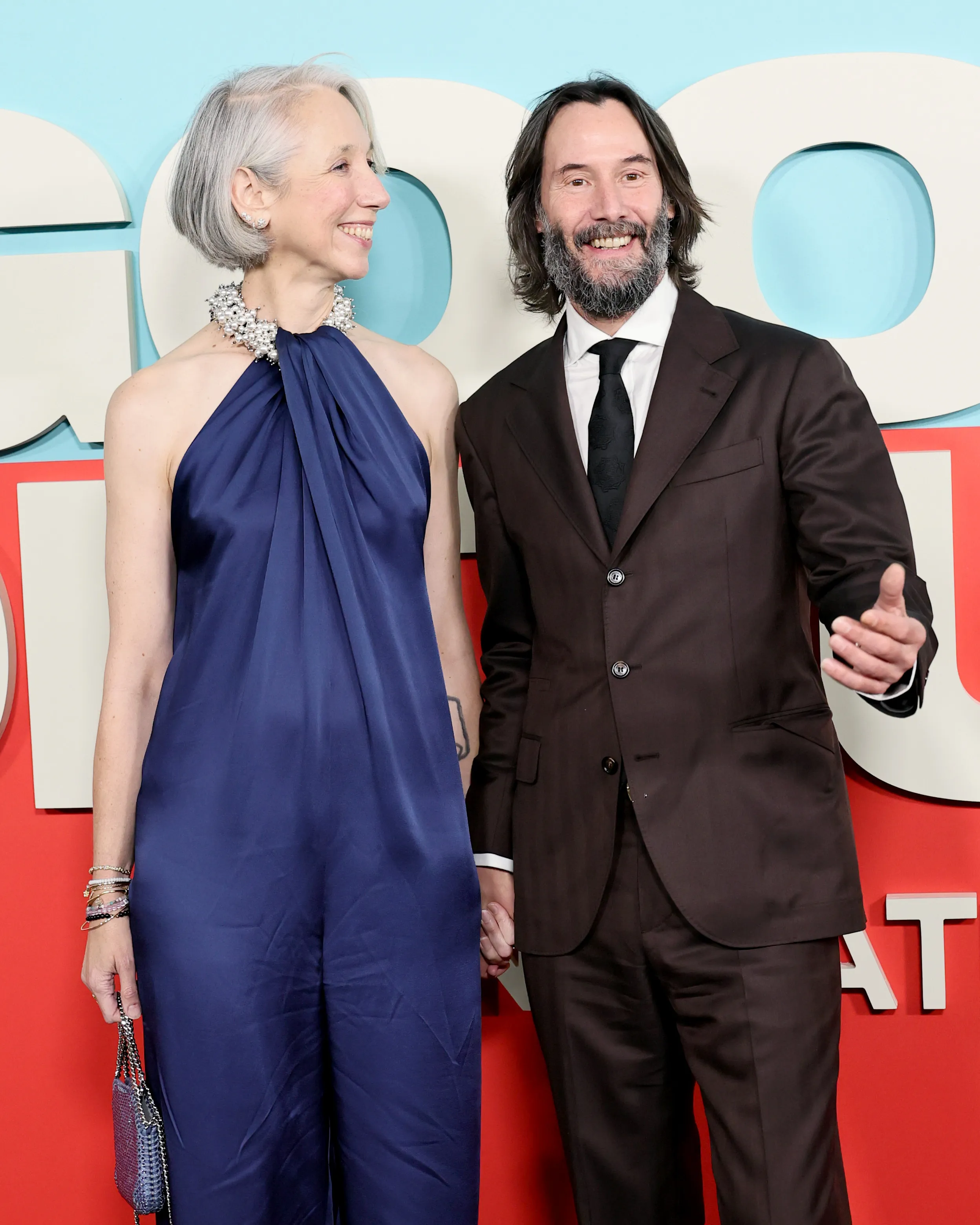 Alexandra Grant in a blue jumpsuit and Keanu Reeves in a brown suit attend the 