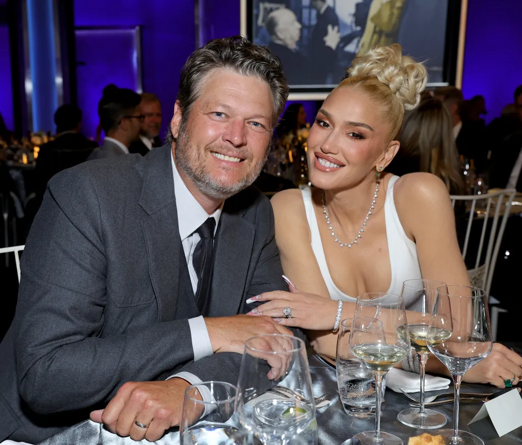 Blake Shelton and Gwen Stefani seated at a formal event, smiling at the camera.