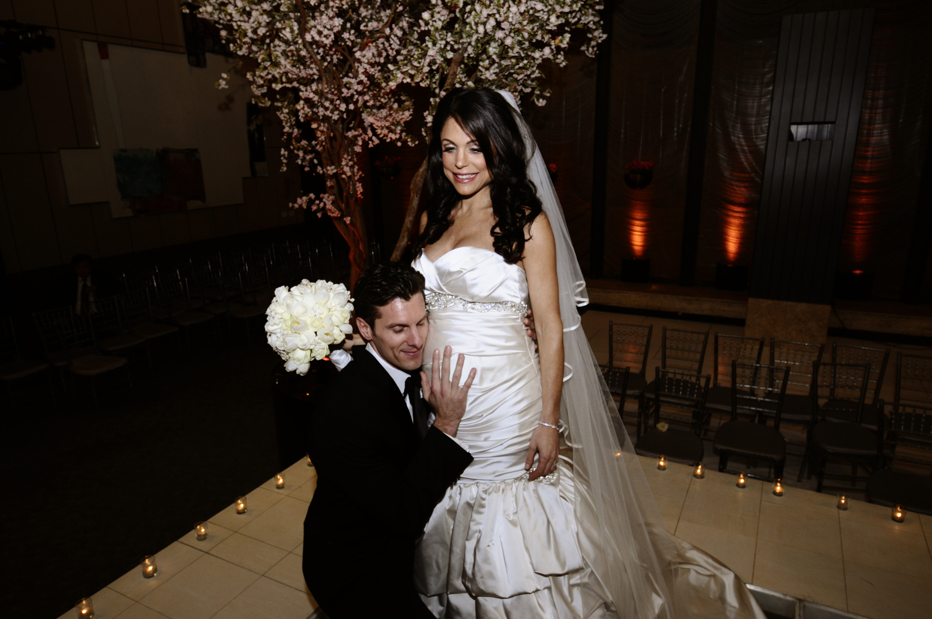 Jason Hoppy kneels and smiles while holding Bethenny Frankel's pregnant belly at their wedding.