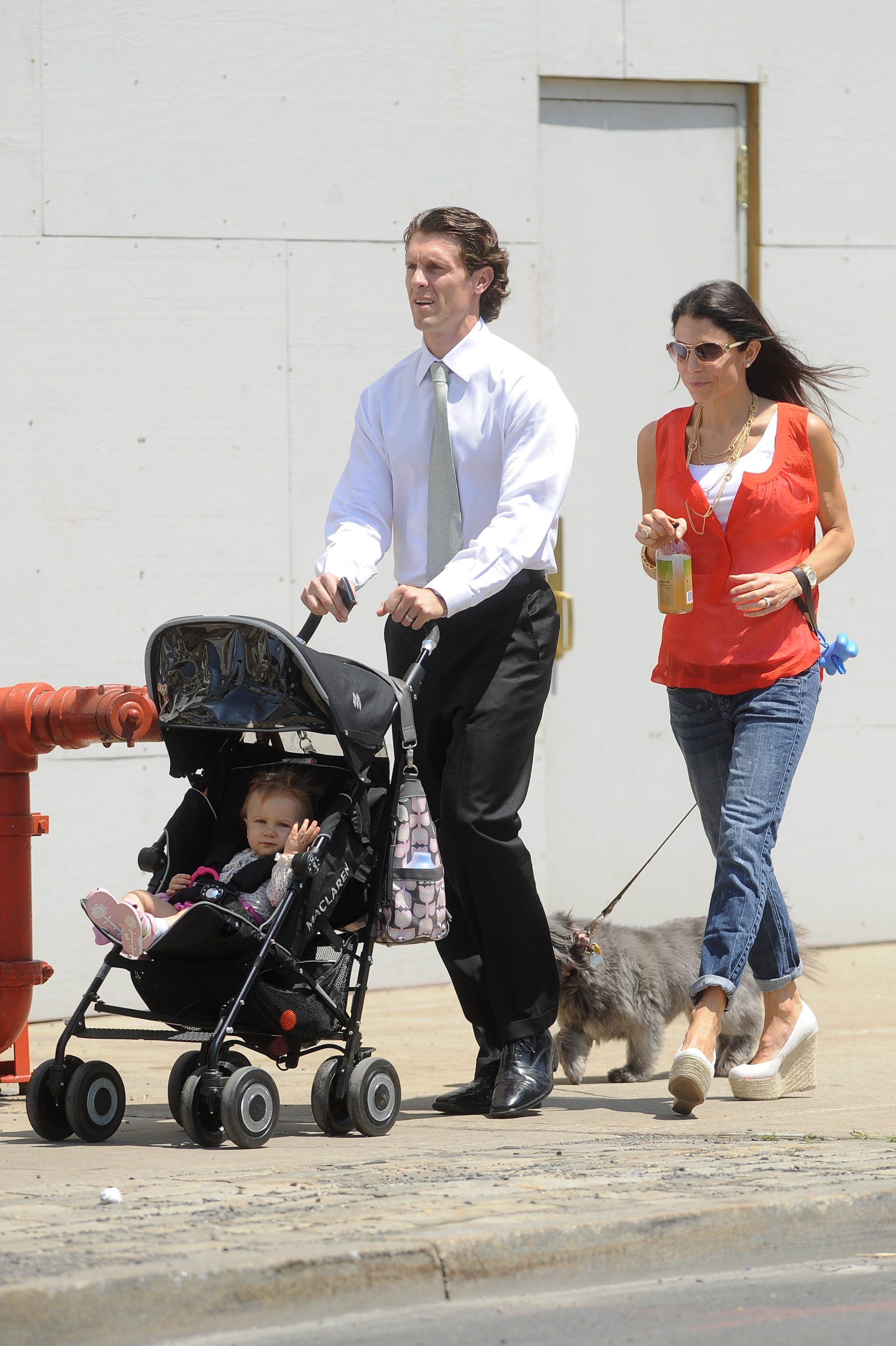 Jason Hoppy pushing Bryn Hoppy in a stroller while Bethenny Frankel walks next to them holding a drink and a dog on a leash.