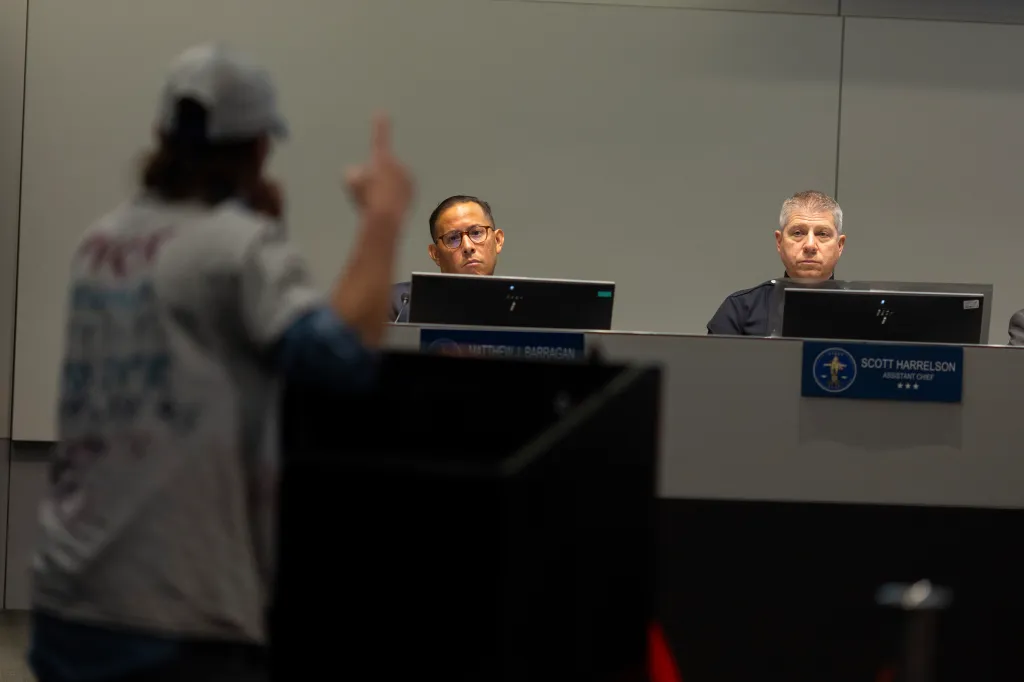 A meeting attendee speaks to LAPD Inspector General Matthew Barragan (left) and LAPD Assistant Chief Scott Harrelson (right) at the Los Angeles Board of Police Commissioners meeting.