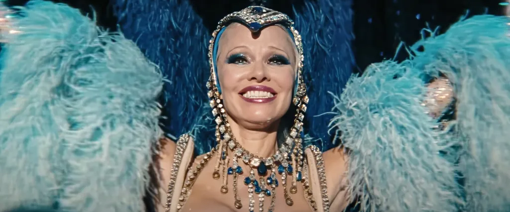 Pamela Anderson as a showgirl in a sparkling costume and feathery blue headpiece.