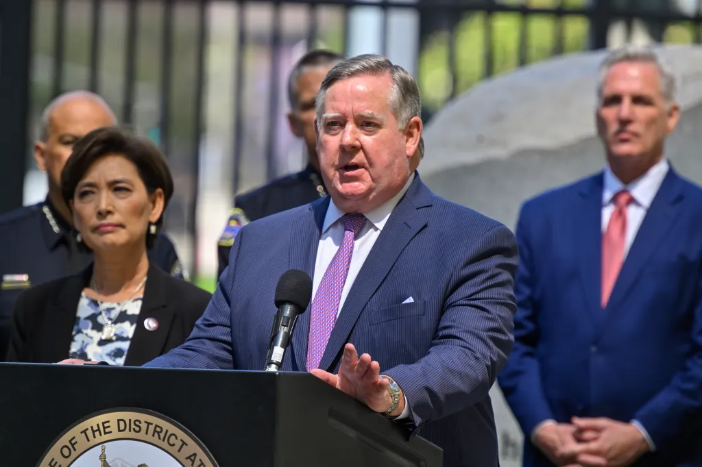 Orange County District Attorney Todd Spitzer speaking at a press conference, with Representative Ken Calvert and other officials in the background.