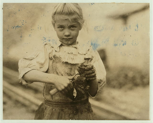 A 7-year-old girl named Rosie, with light hair and a serious expression, shucking oysters with a small tool in her right hand, her hands and clothes covered in grime.