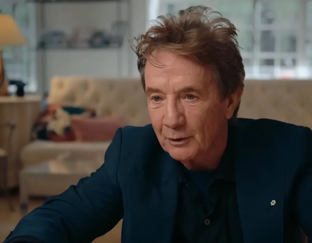 Martin Short in a dark suit with a flower pin on his lapel.